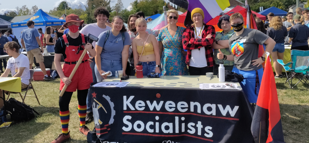 pciture of a group of individuals standing behind a table with a keweenaw socialists banner